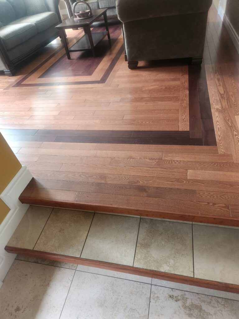Close view of the mixed-species hardwood border where the floor steps down to tile